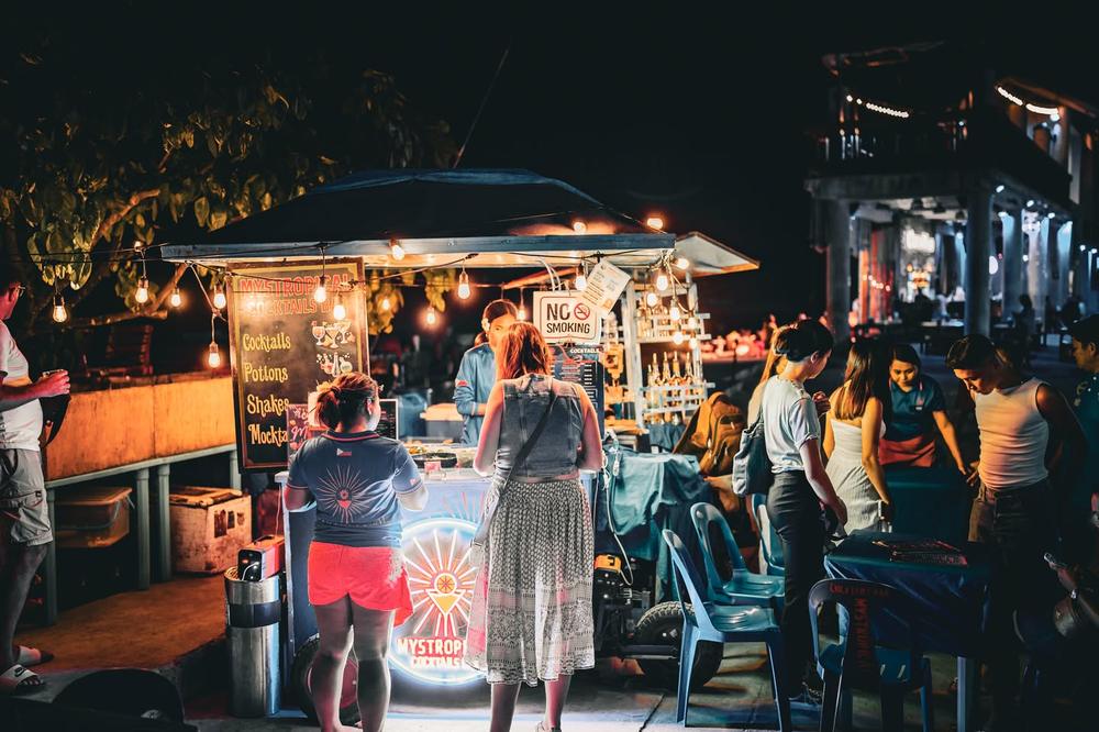 The bar at night, busy with customers around the neon-lit cart